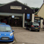 A photograph of the front of Drybrook garage with two blue and one black car parked outside